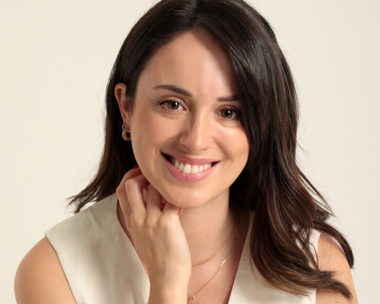 A Dr.ª Vanessa Vieira a sorrir, de mão no queixo, num fundo creme